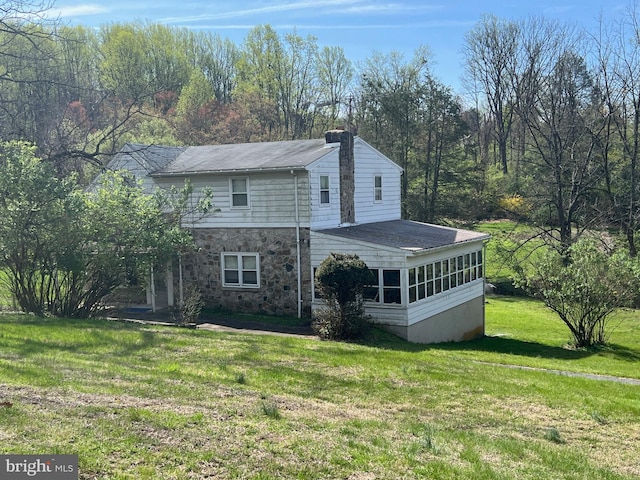 exterior space with a lawn, stone siding, a chimney, and a sunroom