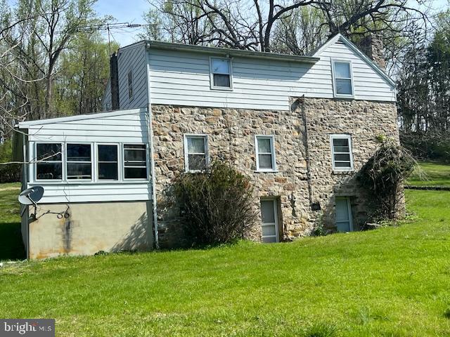 back of house featuring a yard, a chimney, and stone siding