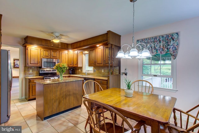 kitchen featuring brown cabinets, stainless steel appliances, light tile patterned flooring, tasteful backsplash, and a center island