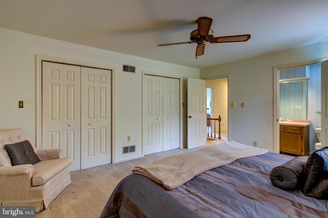 bedroom featuring light colored carpet, ceiling fan, visible vents, multiple closets, and ensuite bath