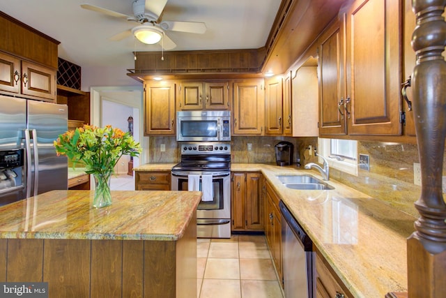 kitchen featuring tasteful backsplash, light stone countertops, stainless steel appliances, ceiling fan, and a sink