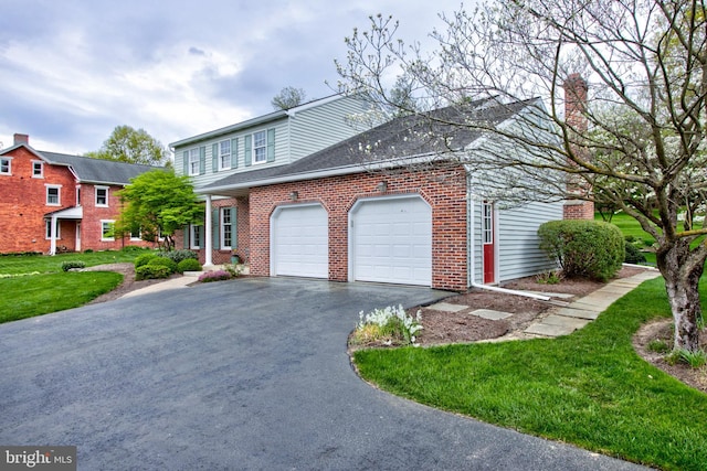 view of front facade with a chimney, brick siding, a garage, driveway, and a front lawn