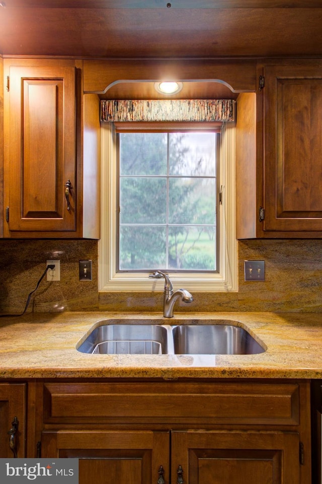 kitchen with light stone counters, a sink, brown cabinets, and tasteful backsplash