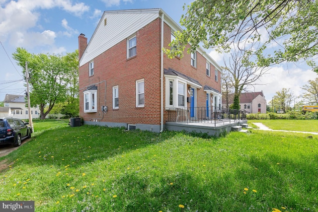 view of home's exterior with cooling unit, a lawn, a chimney, and brick siding