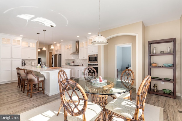 dining room featuring arched walkways, baseboards, recessed lighting, and light wood-style flooring