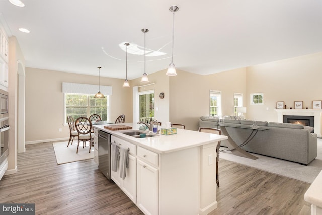 kitchen featuring a kitchen island with sink, light wood-type flooring, white cabinets, a sink, and appliances with stainless steel finishes
