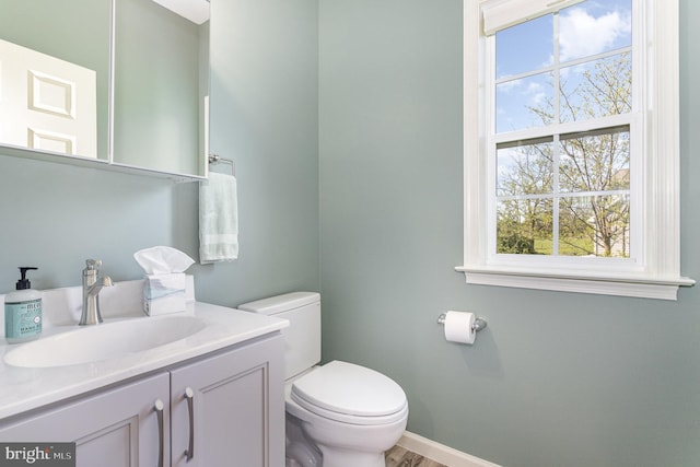 half bathroom featuring toilet, baseboards, and vanity