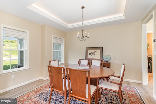 dining space with light wood-style floors, a raised ceiling, baseboards, and a chandelier
