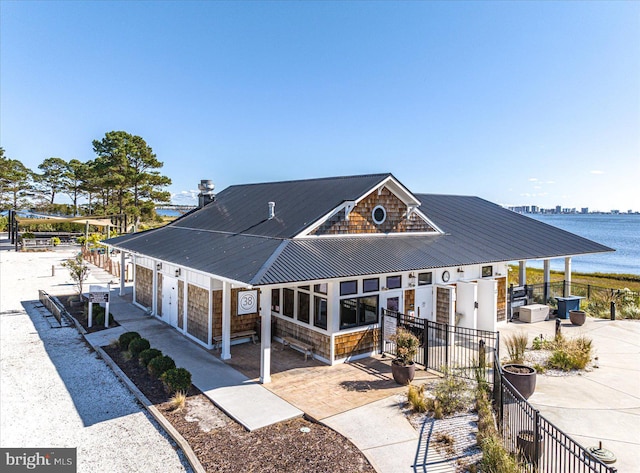 exterior space with fence, a water view, a patio, driveway, and metal roof