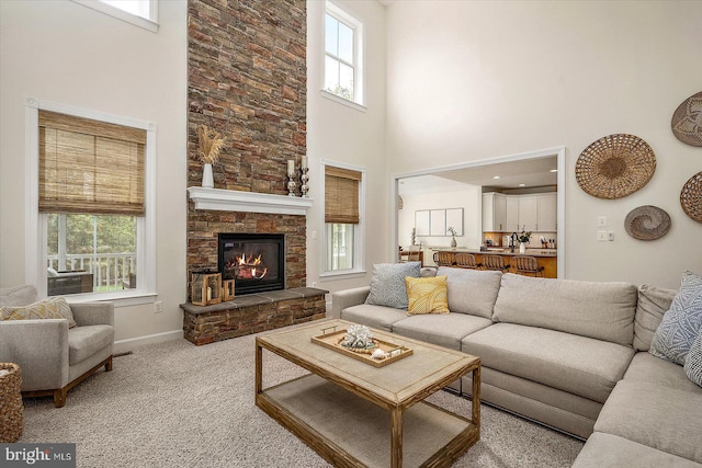 carpeted living area featuring baseboards, a fireplace, and a towering ceiling