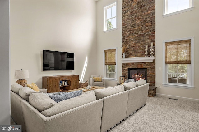 living room with light carpet, a stone fireplace, baseboards, a towering ceiling, and visible vents