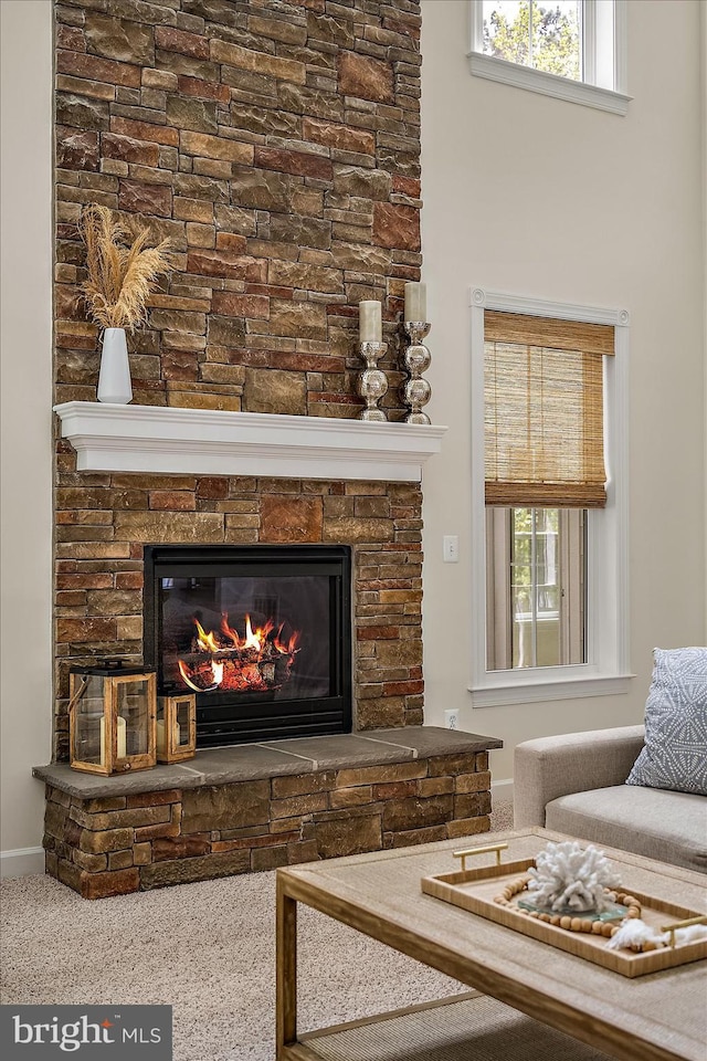 living area with a stone fireplace, baseboards, carpet floors, and a wealth of natural light