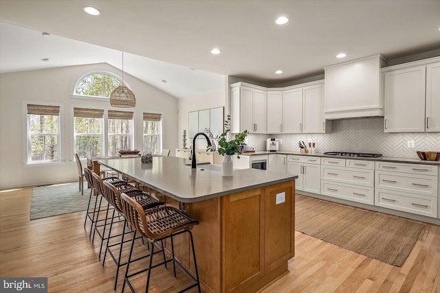 kitchen with light wood-style floors, stainless steel gas cooktop, a center island with sink, and a breakfast bar