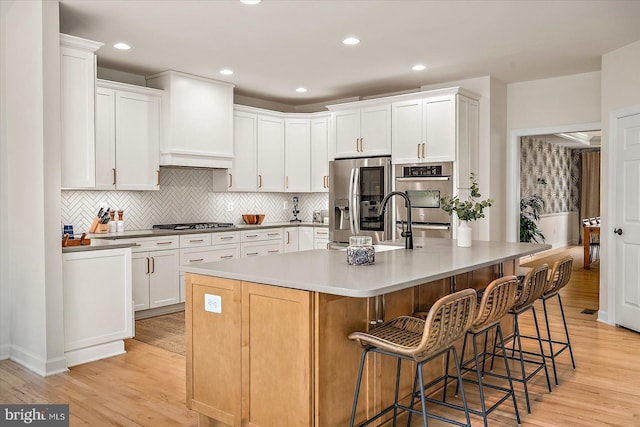 kitchen featuring a spacious island, white cabinetry, light wood-style flooring, backsplash, and stainless steel appliances