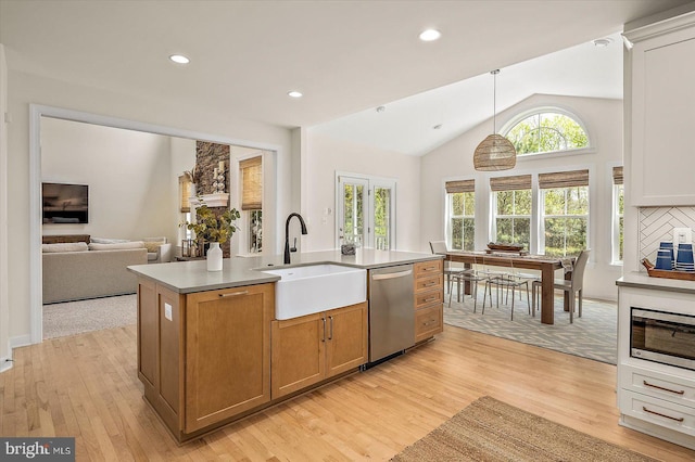 kitchen with appliances with stainless steel finishes, a sink, light wood-style floors, open floor plan, and vaulted ceiling