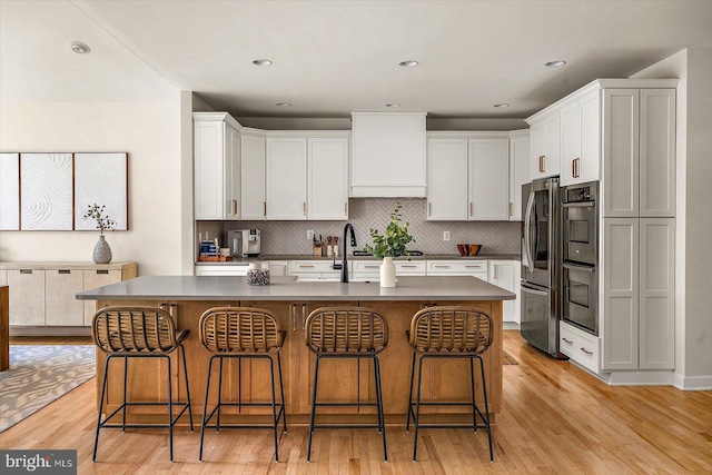 kitchen with tasteful backsplash, stainless steel appliances, a kitchen bar, and light wood-style flooring