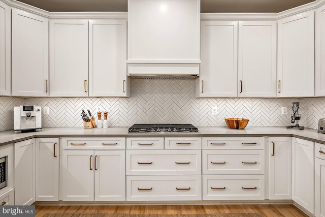 kitchen with stainless steel gas stovetop, decorative backsplash, custom range hood, and white cabinets
