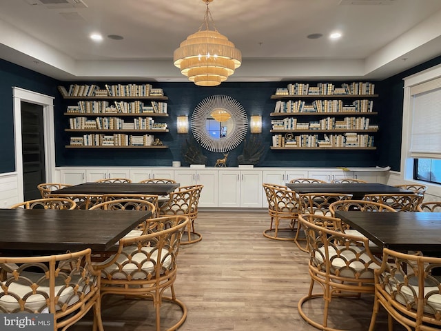 dining room featuring wainscoting, a raised ceiling, a chandelier, recessed lighting, and light wood-type flooring