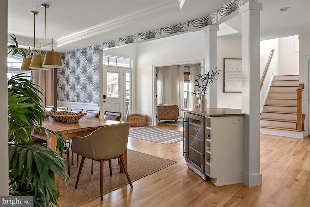 dining space featuring crown molding, stairs, wine cooler, wallpapered walls, and light wood-style flooring