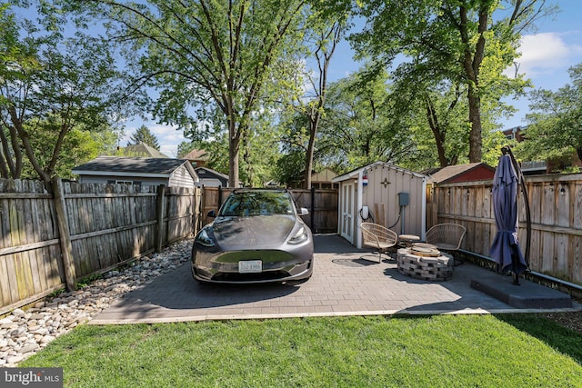 view of yard with a storage unit, a fenced backyard, a fire pit, and an outbuilding