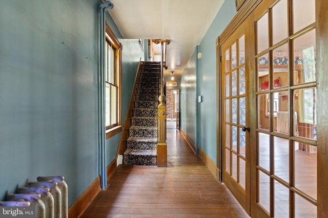corridor featuring baseboards, hardwood / wood-style flooring, french doors, and stairway