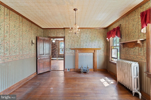 unfurnished dining area featuring crown molding, radiator, wallpapered walls, and hardwood / wood-style floors