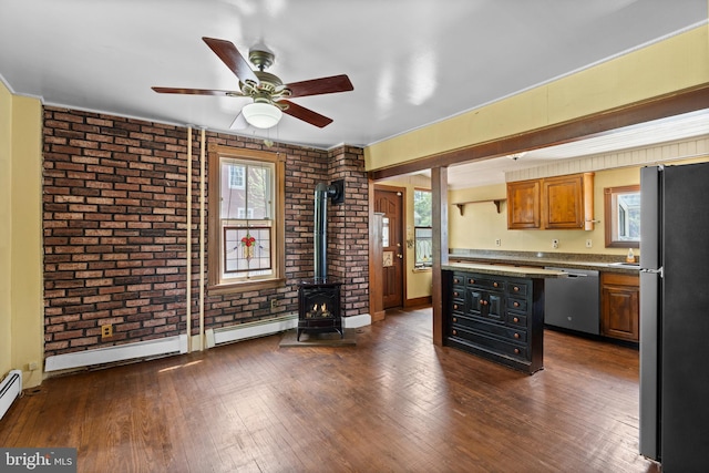 kitchen with a wood stove, brick wall, dark wood-type flooring, a ceiling fan, and appliances with stainless steel finishes