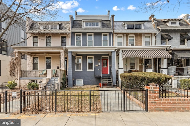 multi unit property featuring brick siding, a porch, mansard roof, and a fenced front yard