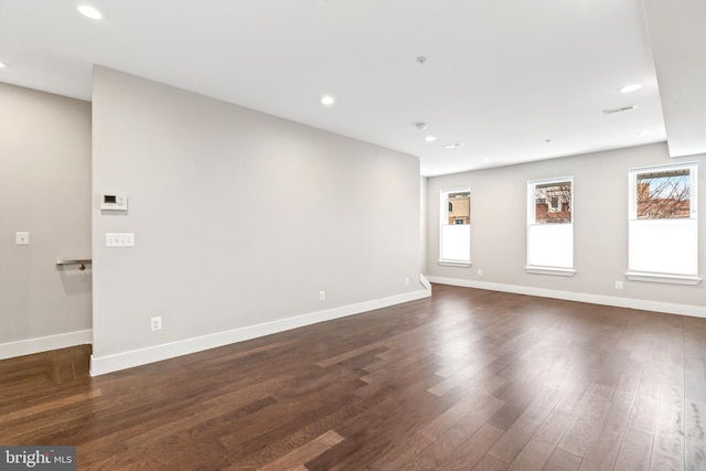 spare room featuring recessed lighting, a wealth of natural light, baseboards, and dark wood-style flooring