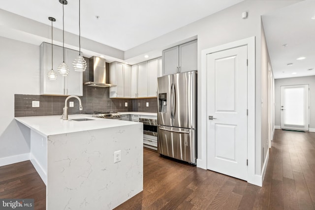 kitchen featuring a sink, wall oven, wall chimney exhaust hood, a peninsula, and stainless steel refrigerator with ice dispenser