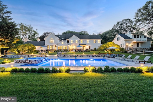 pool at dusk featuring a pool with connected hot tub, a yard, and a patio area
