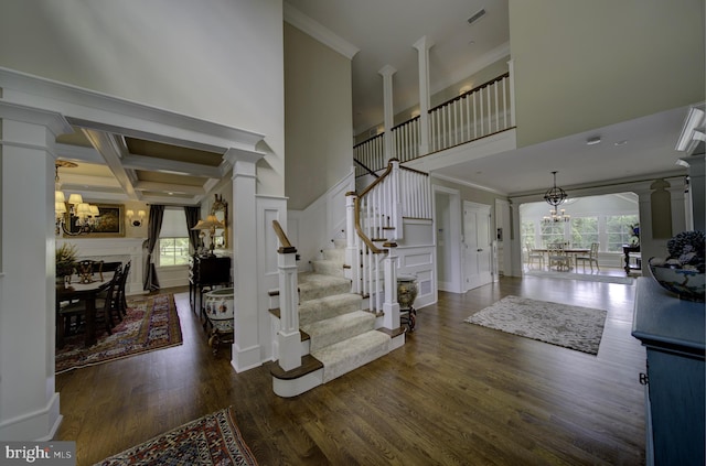 foyer entrance with crown molding, visible vents, ornate columns, and a notable chandelier