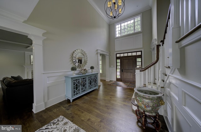 entryway with a high ceiling, an inviting chandelier, a decorative wall, wood finished floors, and ornamental molding