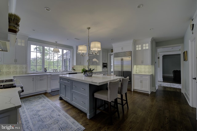 kitchen with a kitchen island, built in refrigerator, light stone counters, backsplash, and gray cabinetry