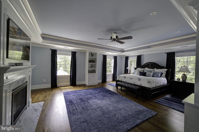 bedroom with ornamental molding, wood finished floors, baseboards, a raised ceiling, and a premium fireplace