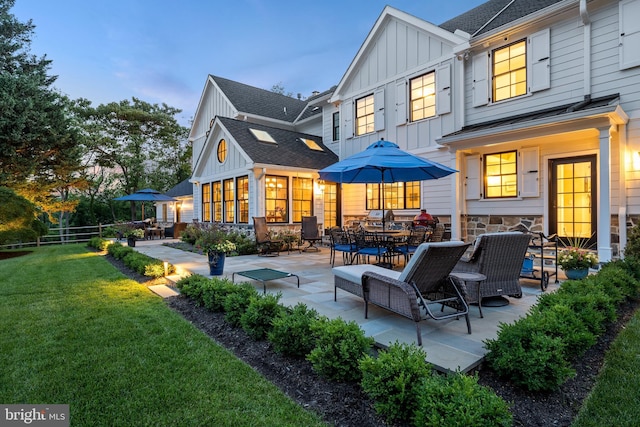 back of property at dusk with fence, roof with shingles, a patio area, board and batten siding, and a yard