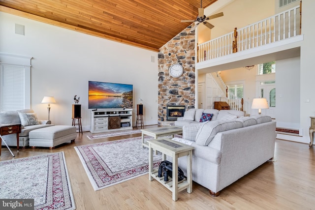 living room with high vaulted ceiling, ceiling fan, a stone fireplace, wood ceiling, and wood finished floors