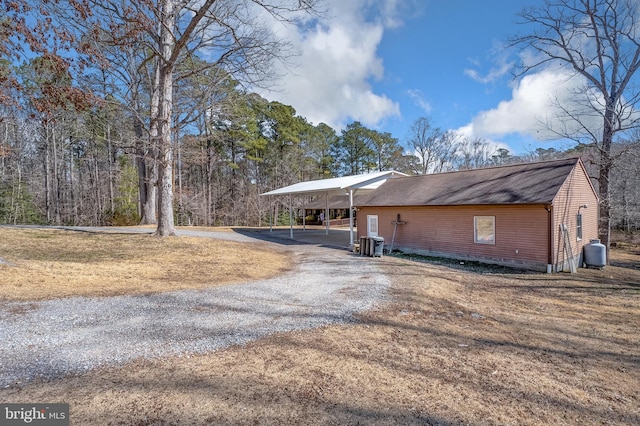 exterior space with central air condition unit, driveway, an attached carport, and roof with shingles