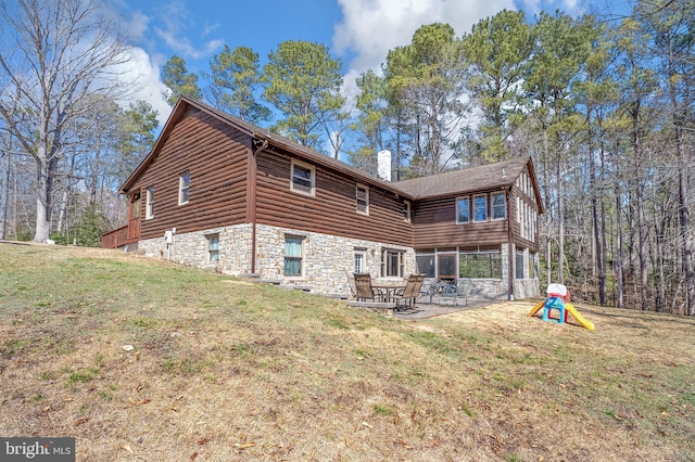 rear view of house featuring a chimney, a patio area, stone siding, and a lawn