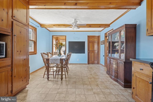dining room with stone finish floor, beamed ceiling, crown molding, baseboards, and ceiling fan