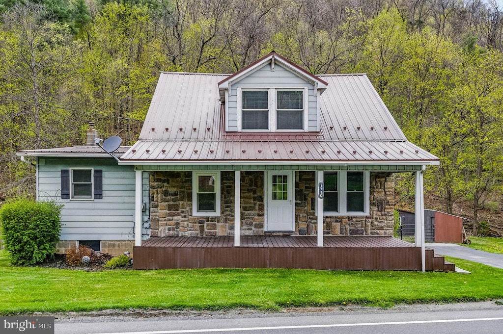 new england style home featuring covered porch, a front yard, a wooded view, and metal roof