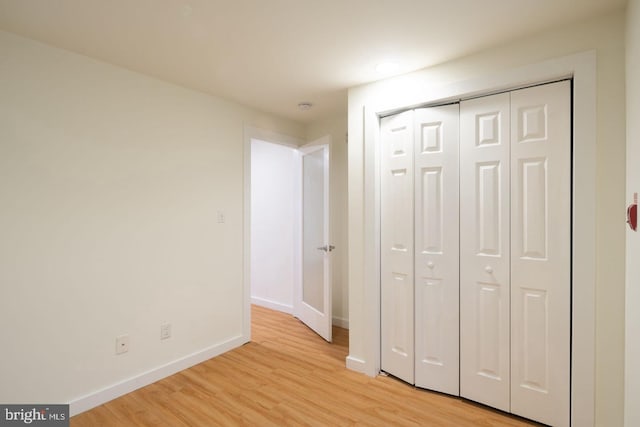 unfurnished bedroom featuring light wood finished floors, baseboards, and a closet