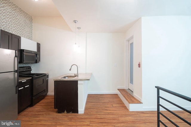 kitchen with a sink, black appliances, light wood finished floors, decorative light fixtures, and baseboards