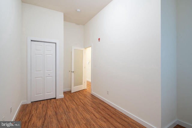 unfurnished bedroom with baseboards, wood finished floors, a towering ceiling, and a closet