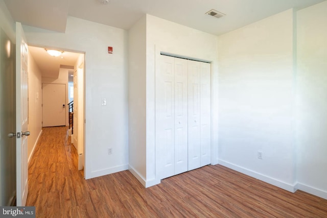 unfurnished bedroom with baseboards, wood finished floors, visible vents, and a closet