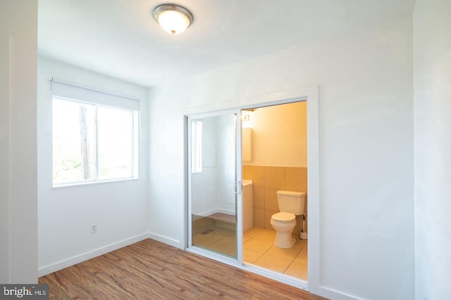 unfurnished bedroom with a wainscoted wall, wood finished floors, ensuite bathroom, and tile walls