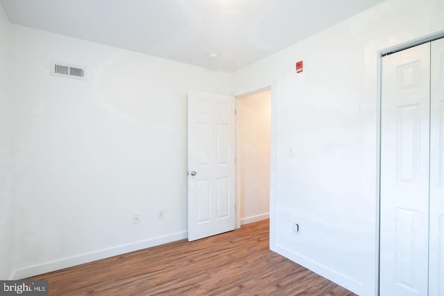 unfurnished bedroom with a closet, wood finished floors, visible vents, and baseboards