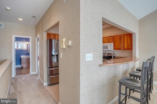 11 Marina View Ct Unit A-6, Bethany Beach, DE 19930 - kitchen with a peninsula, light tile patterned flooring, a breakfast bar area, brown cabinets, and stainless steel appliances