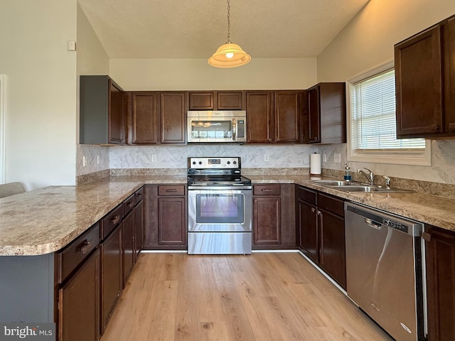 kitchen with appliances with stainless steel finishes, pendant lighting, light wood-style floors, and dark brown cabinets