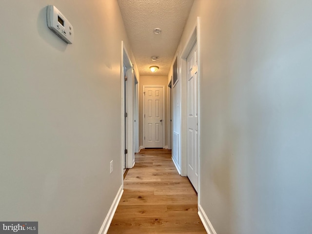 hallway with a textured ceiling, visible vents, baseboards, and light wood-style floors